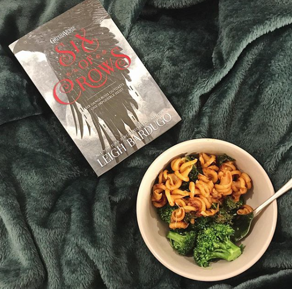Six of Crows by Leigh Bardugo pictured next to pasta with kale and broccoli.